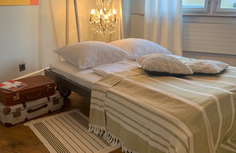 Ferienvermietung Gästebetreuung Mallorca Gemütliches Schlafzimmer mit Bett, Kissen, Teppich und einem alten Reisekoffer. Ferienvermietung Mallorca