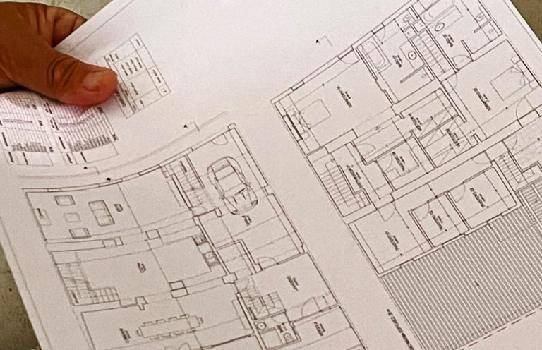 Baubegleitung bei Sanierung und Renovierung von Immobilien auf Mallorca. Hand hält einen Bauplan und Grundriss mit mehreren Räumen. Baubegleitung bei Sanierung und Renovierung auf Mallorca.